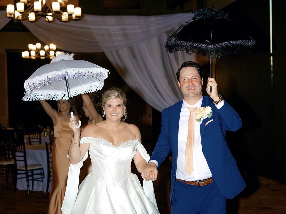 Bride and groom making their grand entrance under fringed parasols beneath a draped reception ceiling